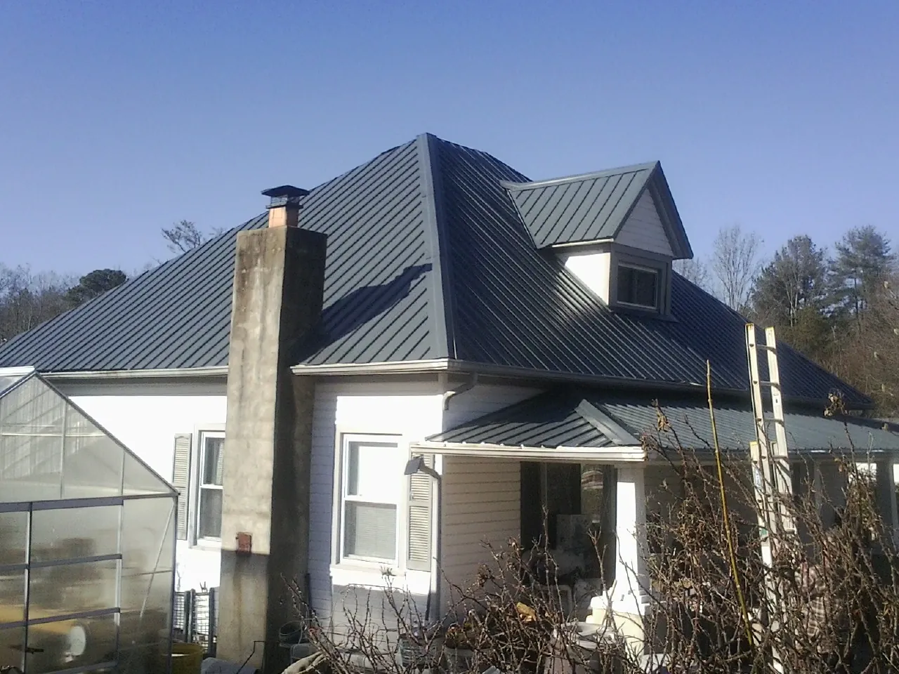 Dark blue standing seam metal roof on a white farmhouse with dormer — Slate & Tile Roof Repair by Roofing Brothers in Corpus Christi