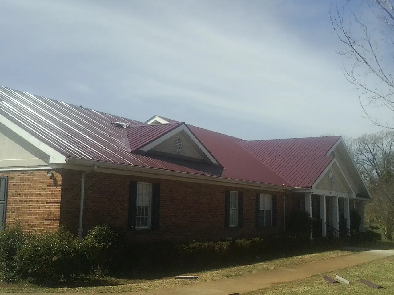 Red metal roof with gabled entries on a long brick building, from a Hail Damage Roof Repair job in Corpus Christi
