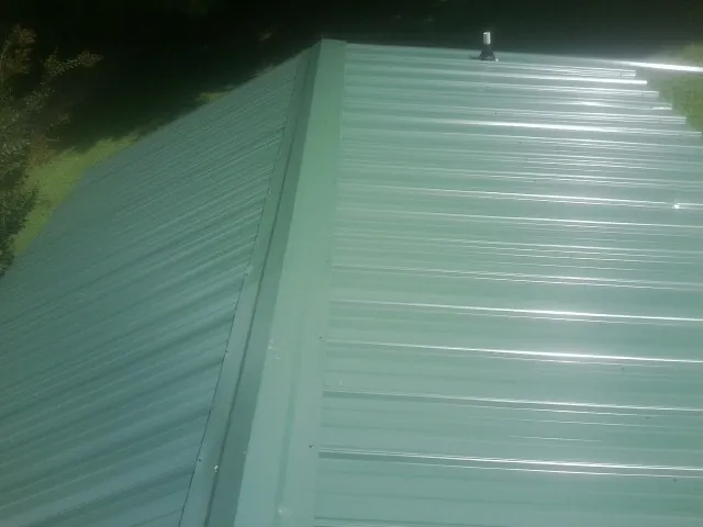 New green metal panels meeting at the ridge of a roof — Flat Roof Repair work by our crew in Corpus Christi