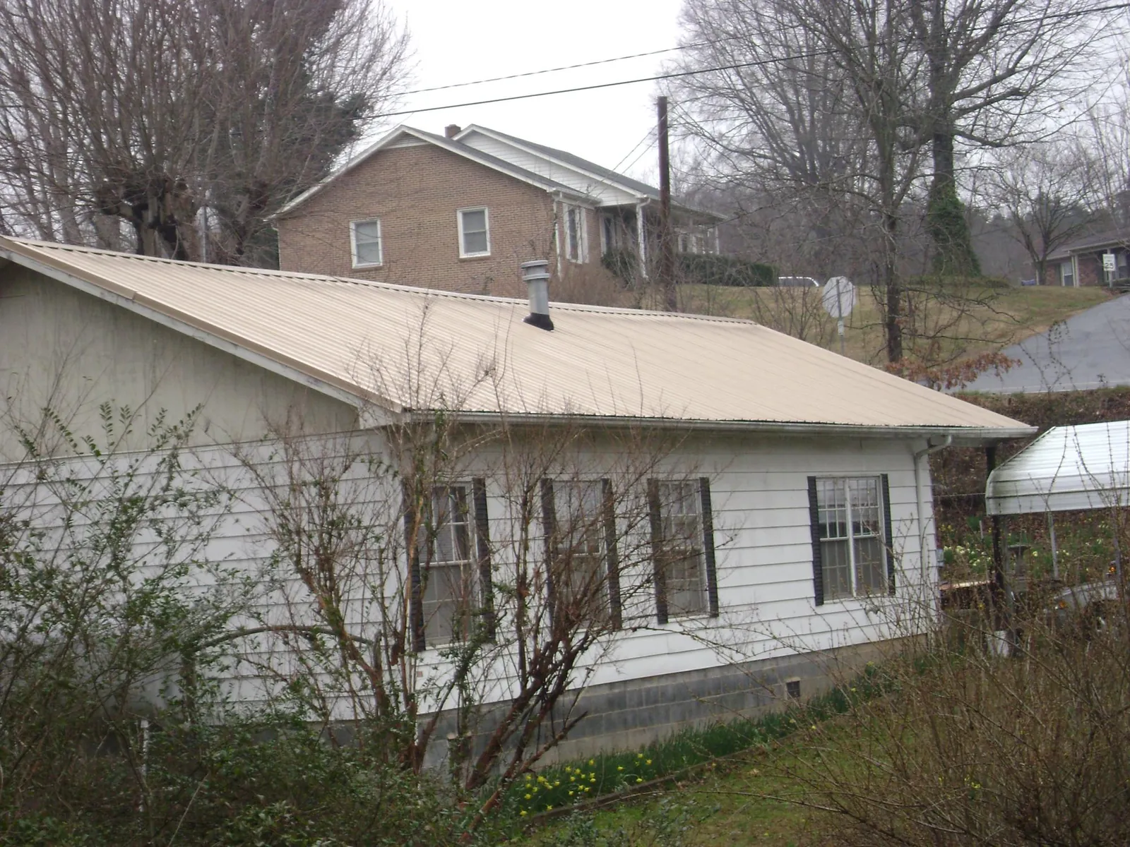 Tan metal roof on a white sided house set into a hillside — Commercial Roofing by Roofing Brothers in Corpus Christi